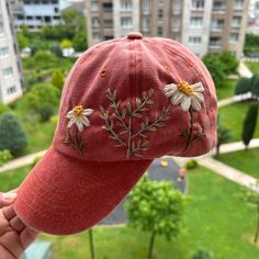 a red hat with daisies embroidered on it in front of a cityscape