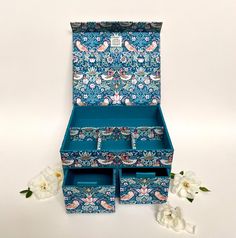 an open jewelry box sitting on top of a table next to flowers and two white roses