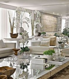 a living room filled with white furniture and lots of plants on top of the coffee table