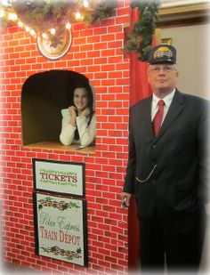 a man in a suit and tie standing next to a fake santa clause train depot