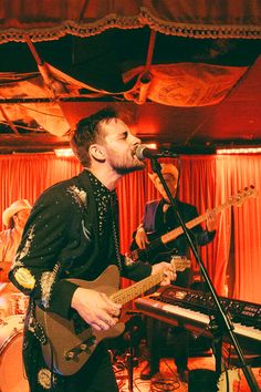 a man singing into a microphone while playing an electric guitar and keyboard in front of him