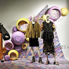 three mannequins dressed in black dresses and jackets stand next to colorful art