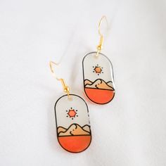 a pair of earrings with mountains and sun on them