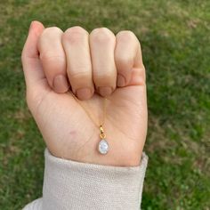 a person holding their hand up to the camera with a small tear shaped pendant on it