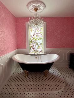 a bath tub sitting under a window next to a black and white tiled bathroom floor