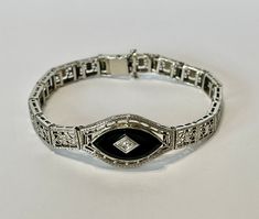 "Gorgeous antique circa 1930s Art Deco era 10k white gold black onyx and genuine diamond bracelet! This phenomenal statement bracelet features intricate bowtie filigree, with a single marquise cut black onyx Gemstone in the center with a 0.11ct genuine diamond. The bracelet secures with a box clasp, and stays secured as it should. A stunning piece of fine Art Deco era jewelry, featuring April's birthstone!  ERA - Circa 1930s - Art Deco  METAL / MATERIAL - 10k white gold, genuine black onyx, genuine diamond  MARKINGS / HISTORY - Bracelet is marked \"10k\"  CONDITION - Good vintage condition. White gold metal has been professionally polished & cleaned. Black Onyx and Diamond are secure in settings. Age appropriate patina & wear remains. Amazing vintage bracelet!  MEASUREMENTS - Length: 6.5 i Art Deco White Gold Bracelets For Evening, Classic Formal Bracelets With Intricate Design, Victorian White Gold Bracelets For Formal Occasions, Victorian Style White Gold Bracelets For Formal Occasions, Art Deco Hallmarked White Gold Bracelets, Art Deco Hallmarked White Gold Bracelet, Classic White Gold Jewelry With Black Enamel, Elegant Collectible Jewelry With Diamond Accents, Antique White Gold Bracelets For Anniversary