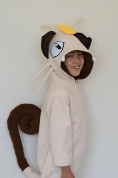 a young boy in a cat costume standing next to a white wall with a monkey on it's back