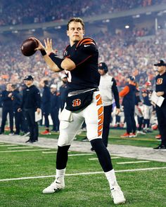 a man holding a football in his right hand on a field with other people watching