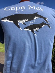 a man wearing a blue shirt with two dolphins on it and the words cape may written in white