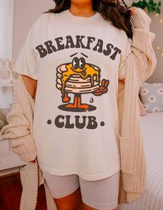 Embrace the joy of mornings with our 'Breakfast Club' tee, where comfort meets whimsy! Crafted from soft, cozy fabric, this shirt features an adorable stack of pancakes, complete with a buttery grin that'll brighten your day. Perfect for lazy brunches or just lounging around, it's a deliciously delightful addition to your wardrobe. Join the club and spread the pancake happiness everywhere you go! White Graphic Print T-shirt For Brunch, Cotton T-shirt With Letter Print For Brunch, White Crew Neck T-shirt For Brunch, Cozy White Graphic Print T-shirt, Cozy Cotton T-shirt With Graphic Print, Crew Neck T-shirt With Screen Print For Brunch, Screen Print Crew Neck T-shirt For Brunch, Funny Print T-shirt For Loungewear, Graphic Tee With Letter Print For Brunch