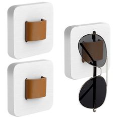 two square shaped sunglasses are hanging on the wall next to each other, and one has a leather case attached to it