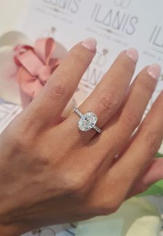 a woman's hand with a diamond ring on top of her finger, next to a pink flower