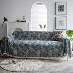 a living room with a couch covered in a blue flowered cover next to a potted plant