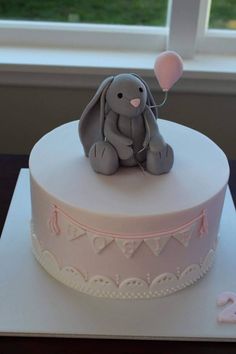 a white cake with an elephant sitting on it's side and a pink balloon in the shape of a heart