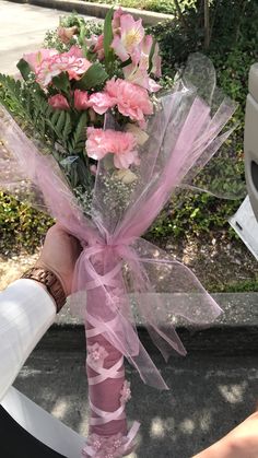 a person holding a bouquet of flowers in their hand with pink ribbons tied around it