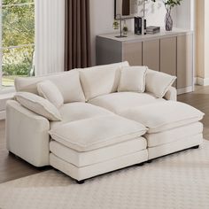 a large white sectional couch in a living room with beige walls and floor to ceiling windows