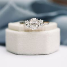 three stone diamond ring sitting on top of a white cloth covered cushioned box with blue fabric in the background