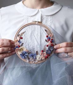 a woman holding a hoop with flowers on it in front of her face while wearing a white dress