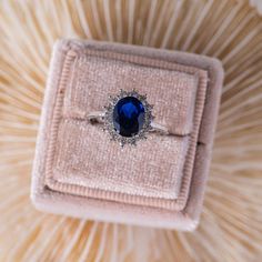 an engagement ring with a blue stone surrounded by white diamonds on top of a pink velvet box