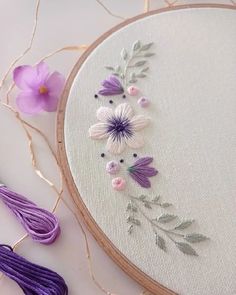 a close up of a embroidery on a white surface with flowers and thread next to it