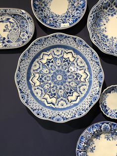 four blue and white plates sitting on top of a black tablecloth covered floor next to each other