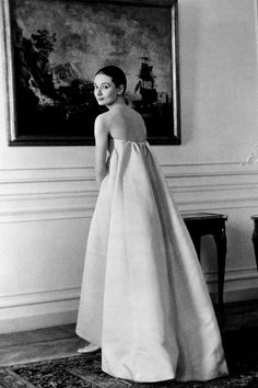 an old black and white photo of a woman in a dress standing next to a painting