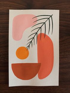 an orange and pink abstract painting on white paper with green leaves in the center, sitting on a wooden surface