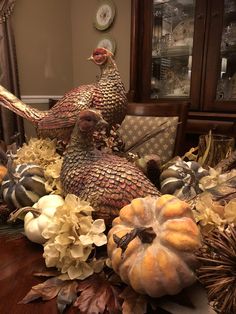 two turkeys sitting on top of a table surrounded by pumpkins and other autumn decorations