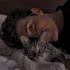 a man laying on top of a bed next to a gray and white cat under a blanket