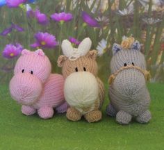 three small knitted animals sitting next to each other on the grass with flowers in the background