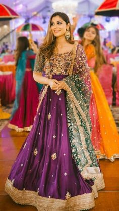 a woman in a purple and yellow dress standing on a wooden floor with other people