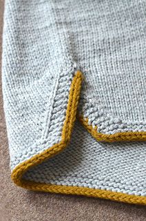 a gray and yellow knitted blanket laying on top of a brown carpeted floor