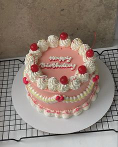 a pink and white birthday cake sitting on top of a cooling rack next to a wall