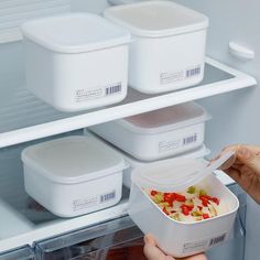 a person holding a container in front of an open refrigerator door with containers on the shelves