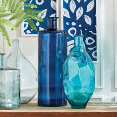 three blue vases sitting on top of a wooden table next to a fern plant