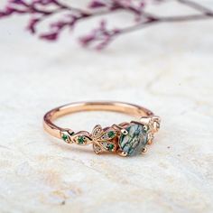 Inspired by nature's delicate beauty, the Moss Blossom ring features a round-cut natural moss agate as the centerpiece, symbolizing the serene connection between earth and art. The band is adorned with petal-like designs on each side, reminiscent of a blooming flower cradling a vibrant green fruit. Each petal is embellished with moissanite, adding a subtle sparkle that enhances the ring’s organic charm. The design seamlessly blends natural inspiration with elegance, perfect for those who appreciate understated sophistication in everyday wear. 𝗗𝗘𝗧𝗔𝗜𝗟𝗦𝗠𝗔𝗜𝗡 𝗦𝗧𝗢𝗡𝗘𝗚𝗲𝗺𝘀𝘁𝗼𝗻𝗲: Natural Moss Agate𝗖𝗼𝗹𝗼𝗿: Green𝗦𝗵𝗮𝗽𝗲: Round 5mm𝗖𝘂𝘁: Full𝗠𝗲𝗮𝘀𝘂𝗿𝗲𝗺𝗲𝗻𝘁: 1.0 ct approx𝗤𝘂𝗮𝗹𝗶𝘁𝘆: VS clarity grademoss agate are natural and can therefore slightly vary in color Moss Agate Round Promise Ring, Elegant Moss Agate Rings With Natural Inclusions, Nature-inspired Emerald Ring For May Birthstone, Nature-inspired Rose Gold Gemstone Rings, Nature-inspired Round Emerald Ring, Nature-inspired Rings With May Birthstone Gemstone, Nature-inspired Rings With Natural Stones For Promise, Nature-inspired Emerald Promise Ring, Nature-inspired Promise Ring With Natural Stones