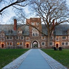 an old brick building with a walkway leading up to the front door and trees on either side