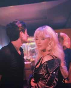 a man standing next to a woman in a black dress and leather jacket at a party