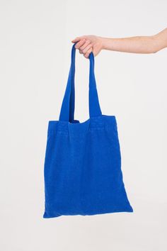 a person holding a blue tote bag in their left hand, on a white background