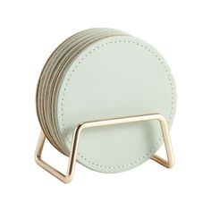 a stack of white leather coasters with gold metal holders on each side and two round plates in the middle