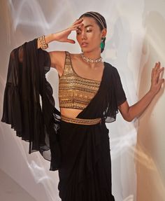 Introducing the stunning Black Ruffled Georgette Saree set seamlessly blends traditional charm with modern sophistication. Crafted from luxurious georgette fabric, the black saree drapes effortlessly, creating a flattering, fluid silhouette. Paired with a meticulously hand-embellished blouse, this ensemble exudes glamour through its intricate detailing. A matching embellished belt cinches the waist, adding a contemporary twist to the classic saree. This style is a ready to wear saree for your ease. Perfect for Cocktails, this outfit truly shines when complemented with statement jewellery and stylish heels. Composition : Saree, Blouse - Georgette Care: Dry Clean Only and Vacuum Storage This product can be customized for sleeves, blouse length and neckline Delivery : 4-6 weeks as the product Party Wear Pre-draped Saree With Cape Sleeves, Elegant Pre-draped Georgette Saree With Zari Work, Elegant Pre-draped Saree With Sheer Dupatta In Georgette, Elegant Pre-draped Georgette Saree With Sheer Dupatta, Elegant Georgette Sharara With Unstitched Blouse, Evening Blouse With Cape Sleeves In Georgette, Evening Georgette Blouse With Cape Sleeves, Draped Georgette Sets For Party Wear, Festive Georgette Sharara With Cape Sleeves