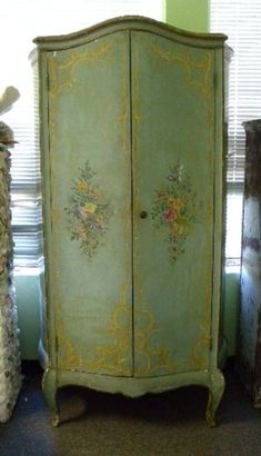 a green armoire with flowers painted on the front and sides, next to a window