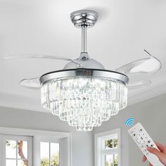 a person holding a remote control in front of a ceiling fan with crystal chandelier