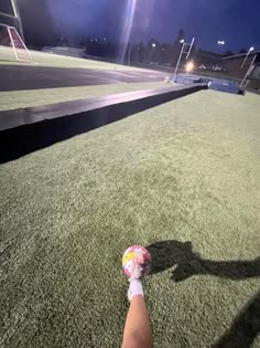 a person's shadow on the ground with a ball in their hand and some lights behind them