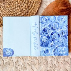 an open book with blue flowers on it next to a straw hat and wooden spoon