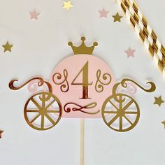 a pink and gold cake topper with a horse drawn carriage on it's side