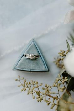 a wedding ring sits on top of a blue napkin next to flowers and greenery