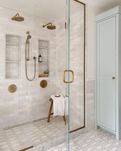 a white tiled bathroom with gold fixtures and glass shower doors, along with an open shelving unit