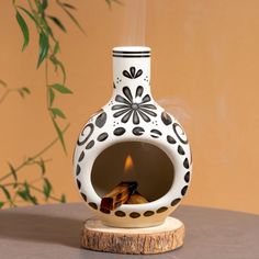 a white and black vase sitting on top of a wooden table next to a plant