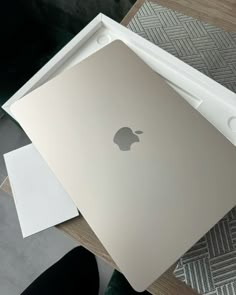 an apple laptop sitting on top of a wooden table next to a white paper tray